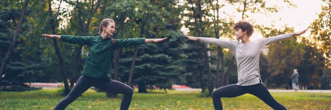 Pretty women is trendy sports clothing are training outdoors doing yoga enjoying movement, fresh air and warm autumn weather. Sports, leisure and youth concept.