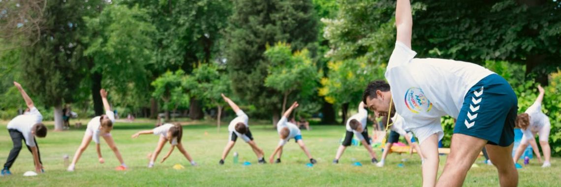 Kids stretching exercises in a park guided by a coach, promoting fitness and fun.